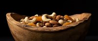 Wooden bowl filled with mixed nuts including almonds, walnuts, hazelnuts and cashews on dark background for healthy snacking and cooking ingredients.