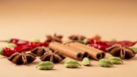 Aromatic spices collection with cinnamon sticks, star anise, cardamom pods and dried chilies scattered on warm beige background for culinary projects.