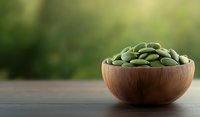 Fresh green pumpkin seeds in wooden bowl on dark table against blurred natural background, healthy organic snack for nutrition and diet.