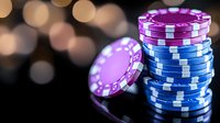 Stack of blue and purple casino poker chips on reflective dark surface with soft bokeh lights in background, dramatic lighting highlights gaming atmosphere.