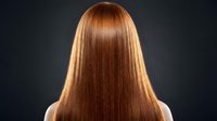 Rear view of a woman with long, straight, glossy auburn hair against a dark background, showcasing healthy, shiny locks after salon treatment.