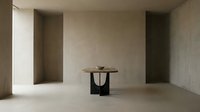 Minimalist interior space featuring a round wooden tabletop supported by a sculptural black base, positioned in a concrete room with recessed wall niches and natural light for modern design projects.