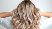 Blonde wavy hair with balayage highlights shown from behind on light background, demonstrating modern hair coloring technique and styling for beauty salon promotion.