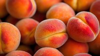 Fresh ripe peaches with fuzzy skin and rosy blush close up, selective focus on juicy summer fruits against dark background, macro food photography.