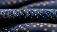 Close up of dark blue denim fabric with golden stitching pattern showing textile texture and weave detail, suitable for fashion and design backgrounds.