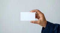 Male hand holding blank white business card against neutral background, ready for branding and corporate design projects.