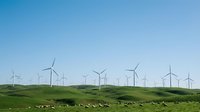Wind turbines on rolling green hills under clear blue sky, renewable energy farm landscape for sustainable power generation.