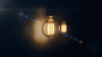 Vintage Edison light bulb glowing with warm filament against dark background with bokeh lights creating atmospheric ambiance for interior design concepts.