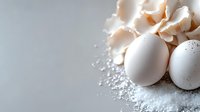 Fresh white eggs with cracked eggshell pieces and flour powder scattered on neutral surface, suitable for baking, cooking, and food preparation projects.