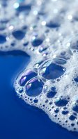 Soap bubbles floating in white foam with iridescent rainbow reflections on blue background for cleaning and hygiene concepts.
