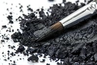 Professional makeup brush with scattered black eyeshadow powder on white surface, close-up view showing texture and detail for cosmetic and beauty concepts.