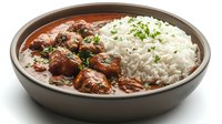 Savory meatballs in rich tomato sauce served with fluffy white rice garnished with fresh herbs in ceramic bowl on white background.