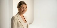 Professional blonde businesswoman in beige suit smiling confidently in modern office setting with natural lighting for corporate presentations.
