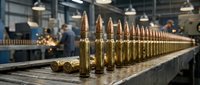 Row of brass ammunition cartridges lined up on metal surface in industrial manufacturing facility with workers in background.