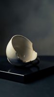 Broken eggshell with soft light casting shadows on dark surface, symbolizing new beginnings, fragility, and transformation for creative projects.