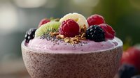 Fresh berry smoothie bowl topped with raspberries, blackberries, kiwi slices, chia seeds and granola in brown ceramic bowl against blurred background.