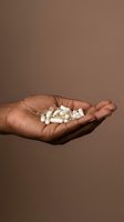 Hand holding white capsule pills and tablets on neutral brown background, representing healthcare, medicine, pharmacy, and wellness treatment options.