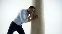 Young Asian businessman in light blue shirt doing wall push-ups exercise in modern office space for workplace fitness and stress relief during break.