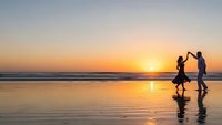 Happy family silhouettes walking on beach at sunset with golden reflections on wet sand. Parents and child enjoying peaceful evening by ocean waves.
