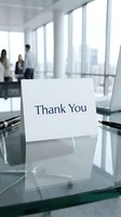 Thank you card standing on a glass desk in a modern office with blurred business professionals and city view in background.