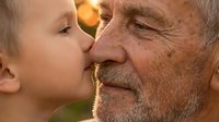 Young child kissing elderly man on cheek in close-up portrait showing intergenerational family bonding and affection between generations.