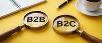 Two magnifying glasses with wooden handles on a bright yellow surface reveal B2B and B2C text, symbolizing business model comparison and market analysis for corporate strategy and sales planning.