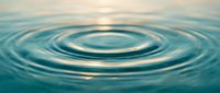 Concentric water ripples spreading across calm turquoise surface with soft golden light reflection creating peaceful aquatic motion pattern for wellness concepts.