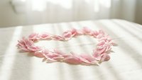 Delicate pink rose petals arranged in romantic heart shape on soft white fabric background for wedding, Valentine's Day, love and romance concepts.