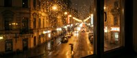 Rainy evening street view through window with glowing lights and wet pavement, urban nighttime scene for backgrounds and atmospheric design projects.