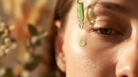 Young woman applying green serum with dropper to face in natural sunlight for skincare routine and beauty treatment.