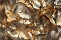 Crumpled metallic gold and silver paper creates dramatic light and shadow play with deep folds and textural details, forming an abstract artistic composition.