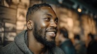 Happy young African American man smiling warmly in casual hoodie at modern cafe or restaurant with blurred background for lifestyle and portrait concepts.