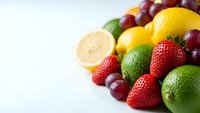 Fresh colorful fruit assortment with strawberries, grapes, citrus and limes on white background for healthy eating and nutrition concepts.