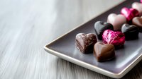 Heart shaped chocolate pralines and truffles on dark ceramic plate against light background, selective focus on luxury handmade confectionery assortment.