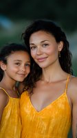 Mixed race mother and daughter wearing matching yellow summer dresses smile warmly at camera, expressing joy and family connection against blurred natural background.