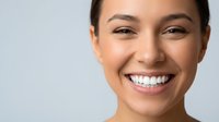Young Hispanic woman with radiant smile showing white teeth, natural makeup and glowing skin against neutral background for dental and beauty concepts.
