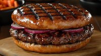 Grilled beef burger with charred marks on glazed bun, topped with red onion rings and sauce, served on wooden cutting board, close-up food photography.