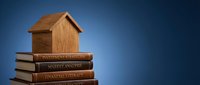 Wooden house model on stack of financial books including investment strategies, market analysis and financial literacy for real estate education concept.