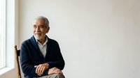 Senior man with gray hair and facial hair, wearing dark blazer over light shirt, seated by window in professional portrait setting for business and corporate use.