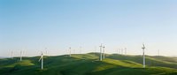 Renewable energy wind turbines dotting rolling green hills under clear blue sky, representing sustainable power generation and clean technology for environmental conservation.