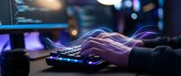 Professional gamer hands typing on illuminated gaming keyboard with colorful RGB lighting effects in dark gaming setup with multiple monitors.