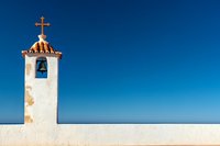 White church bell tower with cross against deep blue sky, minimalist Mediterranean architecture style composition with clean lines and copy space.