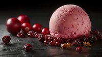 Pink ice cream scoop with scattered dried cranberries and fresh red berries on dark stone background, dramatic food photography with selective focus.
