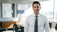 Professional businessman in white shirt and tie smiling confidently in modern office workspace with natural lighting for corporate communications.