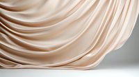 Elegant flowing beige silk fabric with soft waves and folds creating gentle curves and shadows against neutral background, luxury textile with smooth satin texture.
