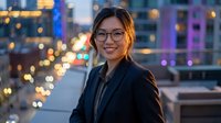 Young Asian businesswoman with glasses smiling confidently in modern city at night with colorful bokeh lights and urban skyline background for corporate success.