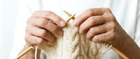 Elderly hands knitting cream wool yarn with wooden needles, crafting a cable stitch pattern, close-up view of traditional handmade textile hobby.