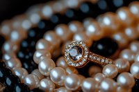 Elegant diamond engagement ring with halo setting nestled among lustrous white pearls and black onyx beads, captured in romantic macro photography.