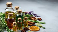 Natural essential oils in glass bottles with cork stoppers, fresh herbs, dried orange slices and spices for aromatherapy and wellness treatments.