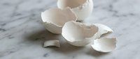 Broken white eggshells scattered on marble surface creating organic fragments and natural textures for cooking and kitchen concepts.